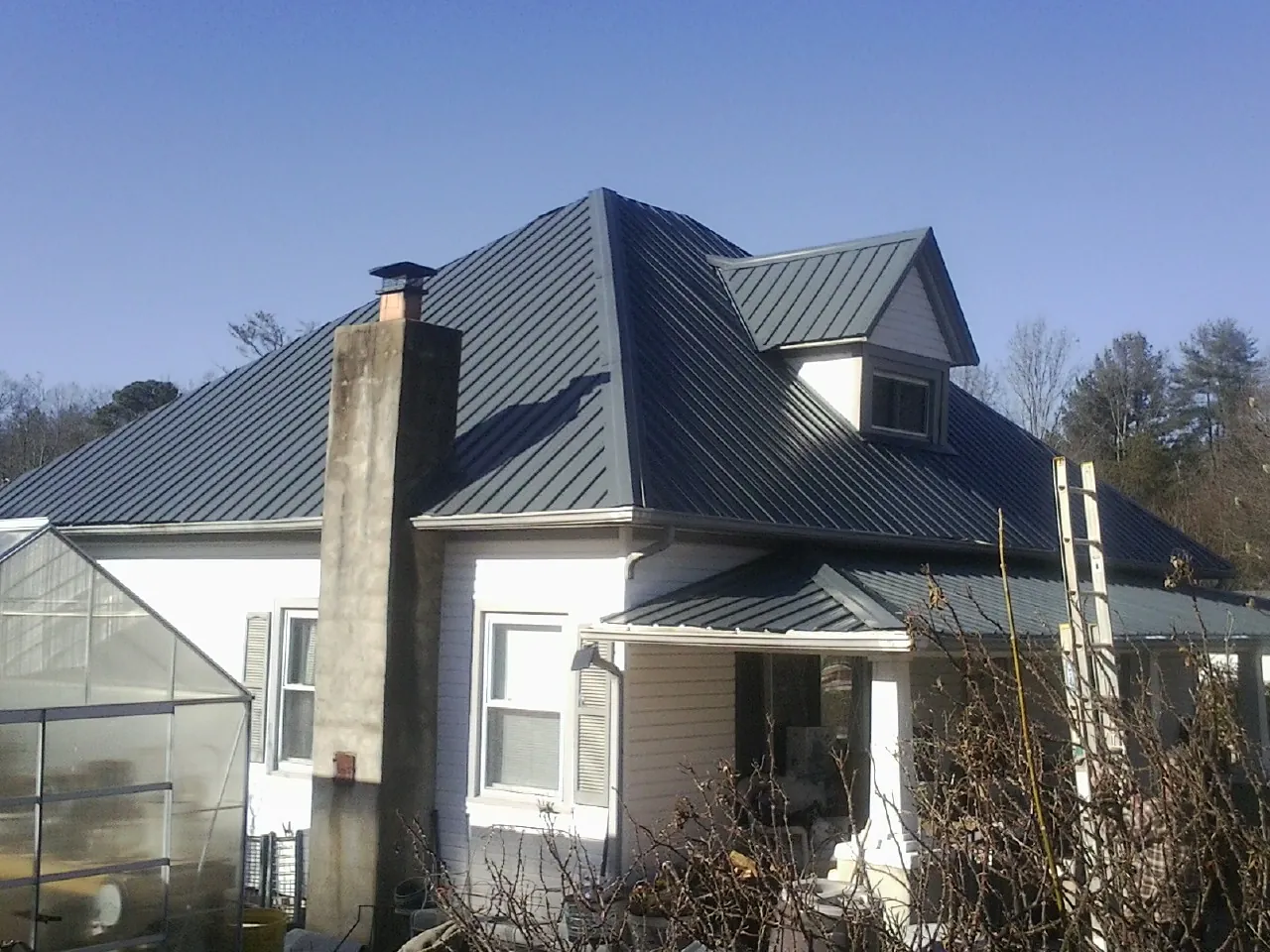 Dark blue standing seam metal roof on a white farmhouse with dormer — Slate & Tile Roof Repair by Roofing Brothers in Prince Frederick