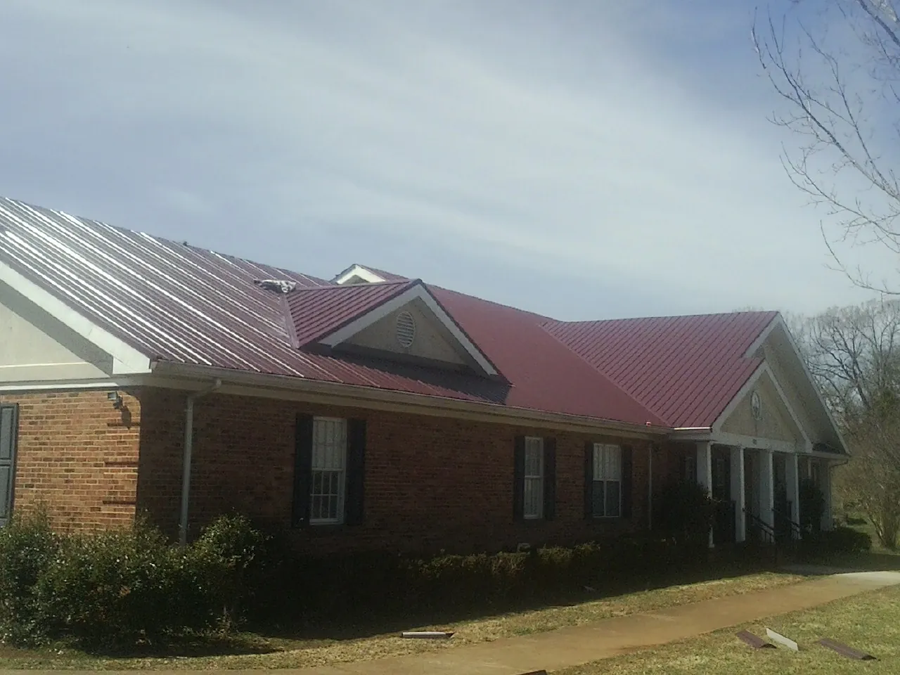 Red metal roof with gabled entries on a long brick building, from a Hail Damage Roof Repair job in Prince Frederick