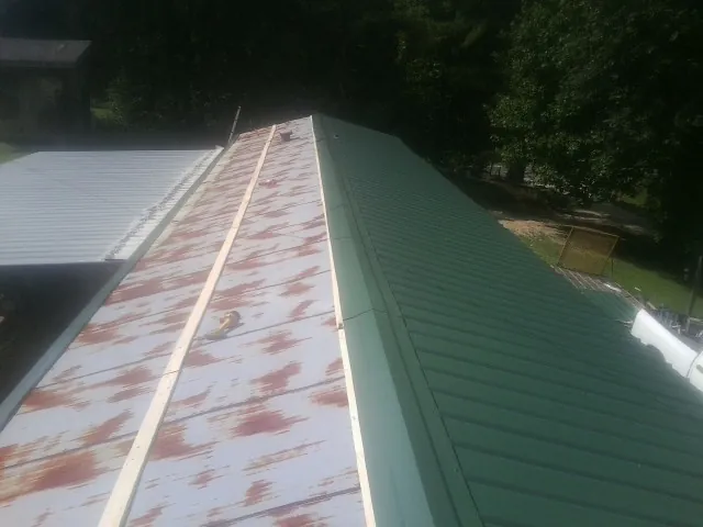 Old rusted panels beside newly installed green metal roofing — Wind Damage Roof Repair by Roofing Brothers in Prince Frederick