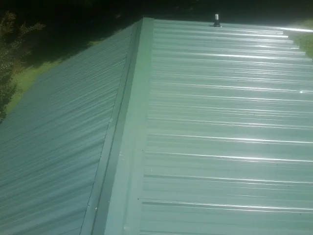 New green metal panels meeting at the ridge of a roof — Flat Roof Repair work by our crew in Prince Frederick