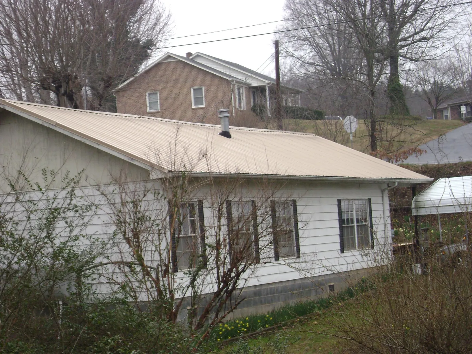 Tan metal roof on a white sided house set into a hillside — Commercial Roofing by Roofing Brothers in Prince Frederick