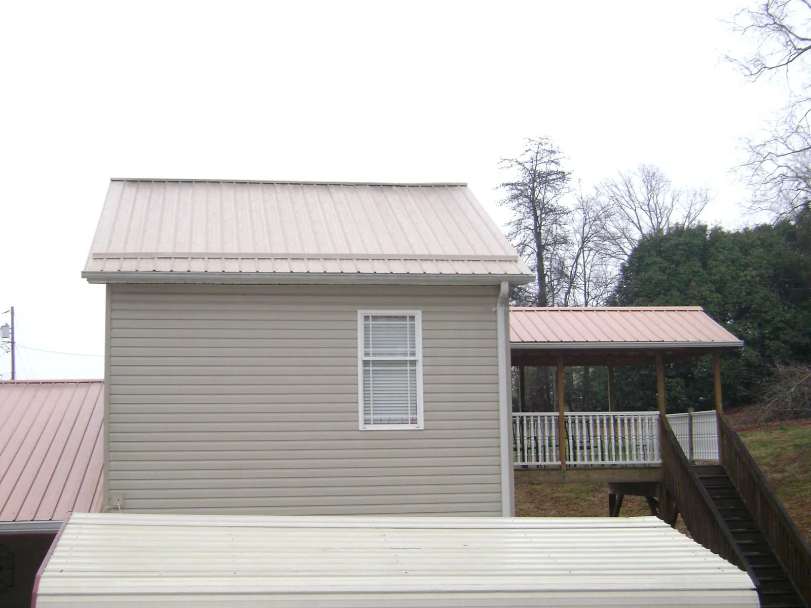 Tan metal roofs on a two story addition and attached porch, from a Roof Replacement job in Prince Frederick
